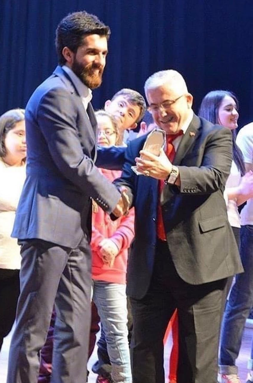 Ödül takdimi sırasında önde duran iki kişi, el sıkışma ve ödül