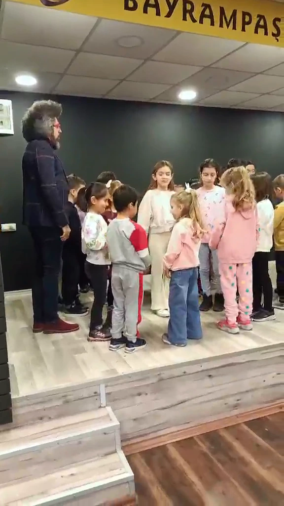 Çocuklar atölyede grup hâlinde hareket ediyor ve eşleşiyor; İlyas Çağlayan çalışmayı yönlendiriyor